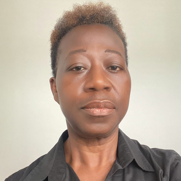 davina-boakye-02 A woman with short hair and a neutral expression wears a black shirt, with a plain, light background. No landmarks or buildings visible.