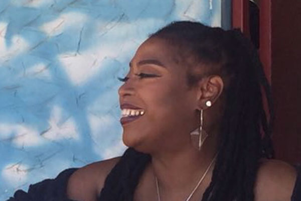 A person with long hair and earrings smiles against a blue textured background, creating a lively and cheerful atmosphere.