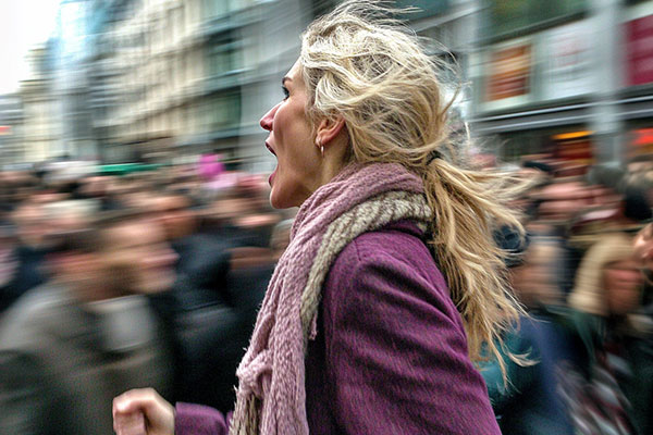 A person in a purple jacket moves swiftly through a busy crowd on an urban street, with motion blur effect enhancing the sense of speed.